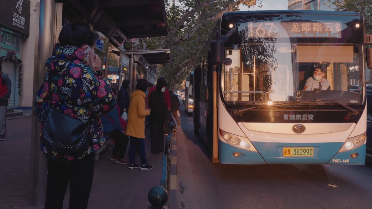 A busy bus stop in Shanghai, China where all passengers are wearing masks. People are getting on a bus.