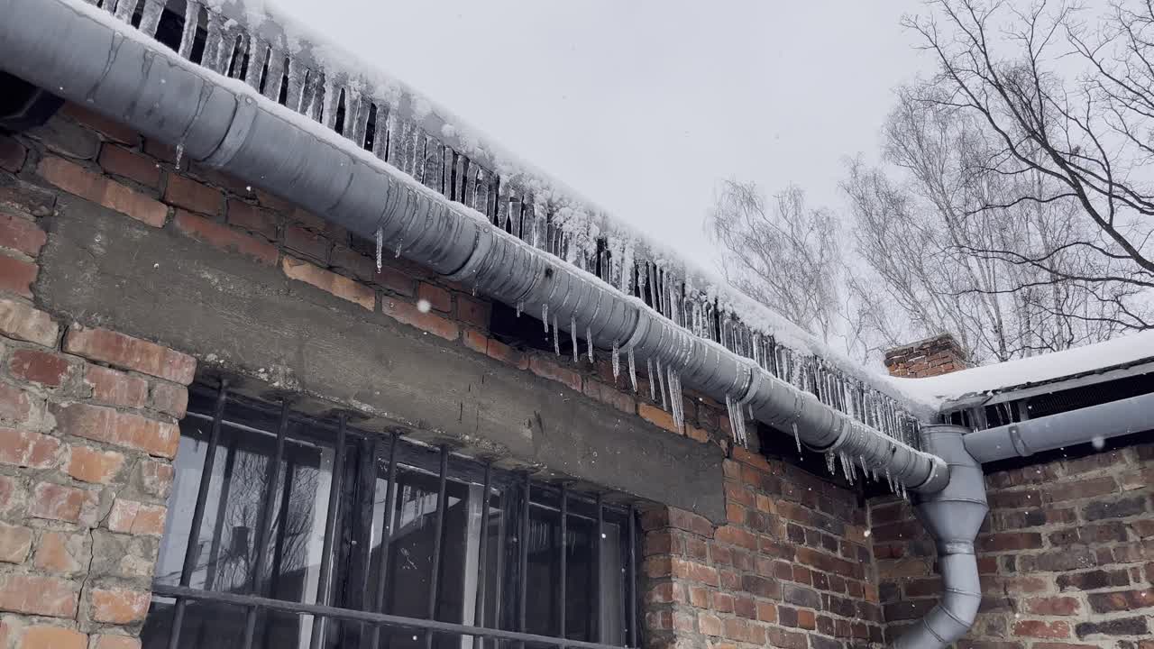 Icicles hanging from roof in Auschwitz Camp 1 - winter with snow falling