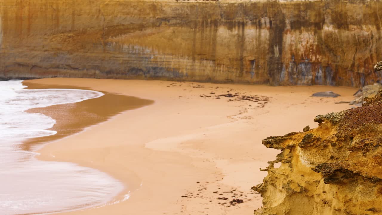 Waves gently lap against sandy cliffs