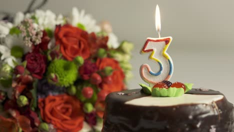 dolly: flower arrangement and birthday cake with burning candle number 3