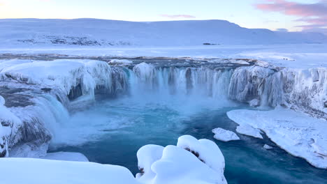 fast flowing water over the godafoss waterfalls in a snowy landscape in iceland after sunset