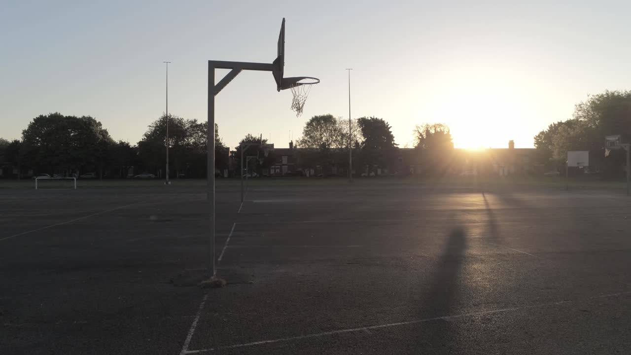 Silhouette in ombra all'alba su un campo da basket vuoto, carrellata bassa a destra