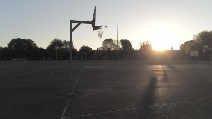 Silhouette in ombra all'alba su un campo da basket vuoto, carrellata bassa a destra