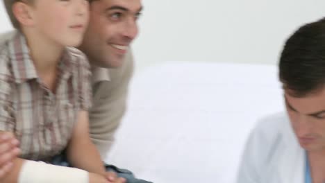 médico vendando el pie de un paciente con su padre en el consultorio médico
