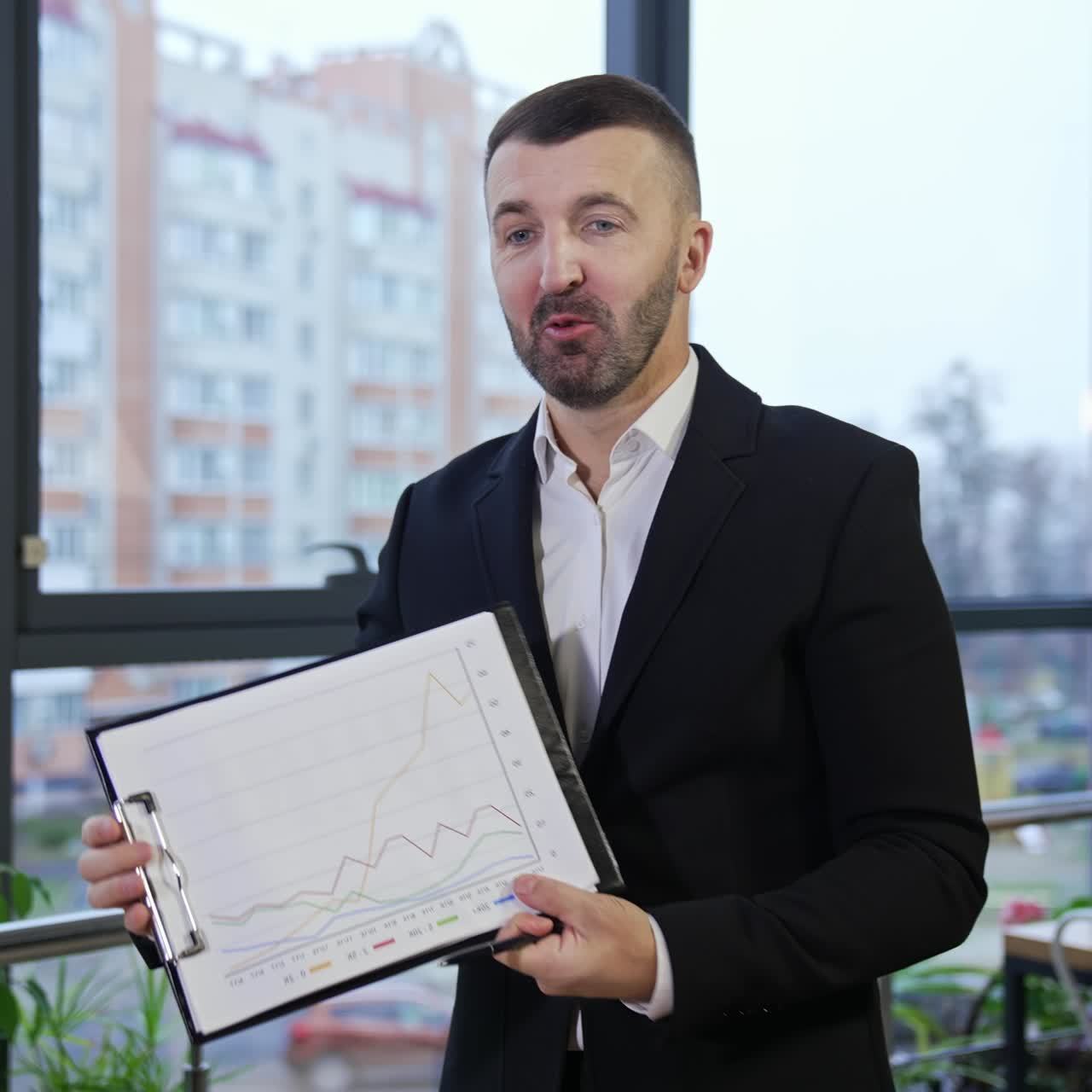 Businessman wearing suit talking to business colleagues or partners sitting at conference table. Male leader holding a folder in his hands showing a chart to his colleagues