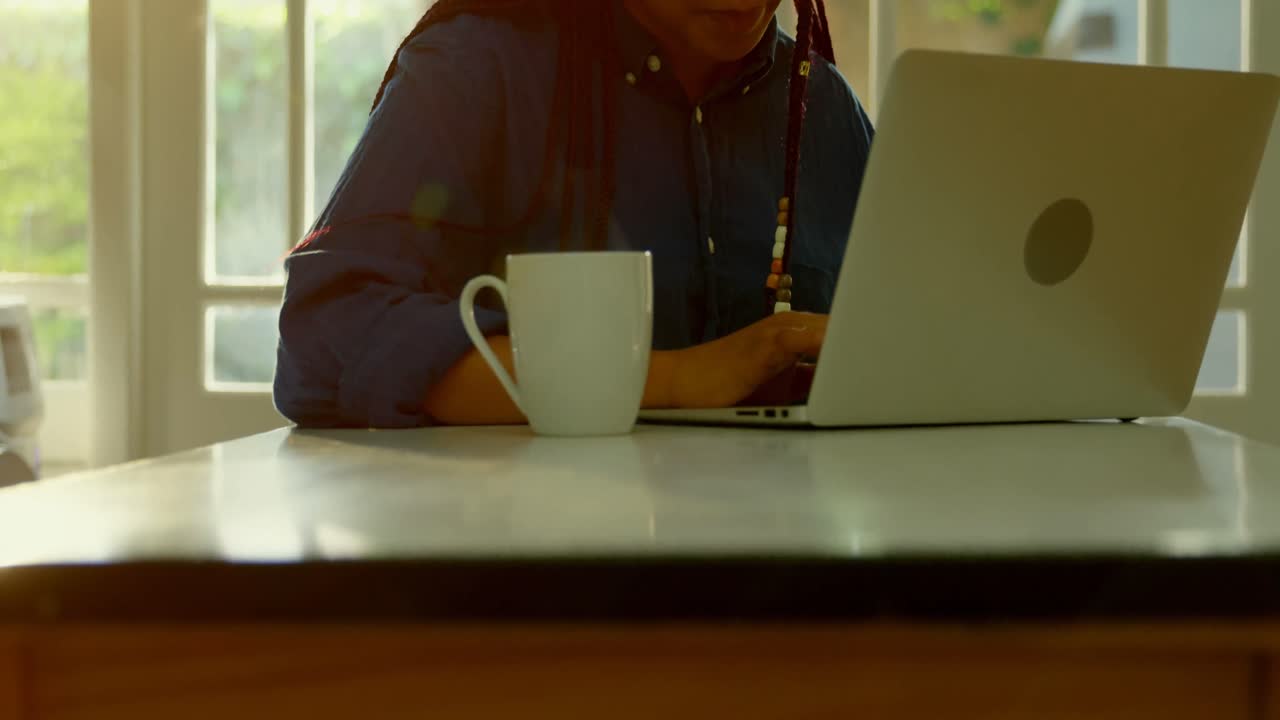 vista frontal de una joven negra trabajando y sentada en la mesa de comedor en un cómodo hogar 4k