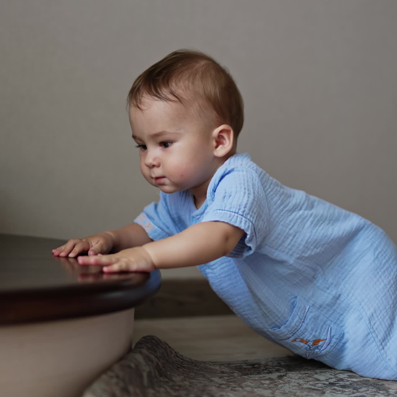 Cute adorable baby in blue romper crawls by the floor to the stairs. Beautiful child wants to get a toy from the stair