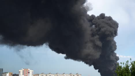 black smoke rises above the buildings. a big chemical fire at a factory building. thick black smoke covers the sky.