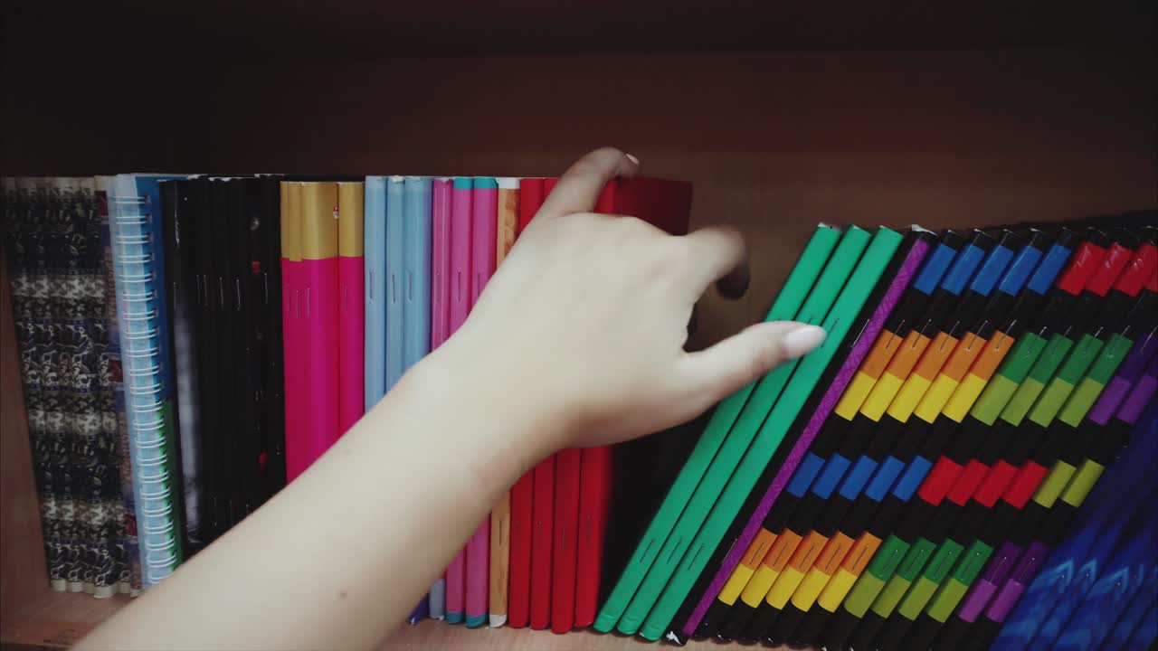 mano alcanzando un libro en una estantería de libros colorida
