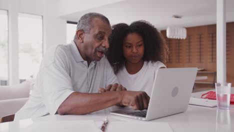 adolescente negra ayudando a su abuelo a usar una computadora portátil en casa, de cerca