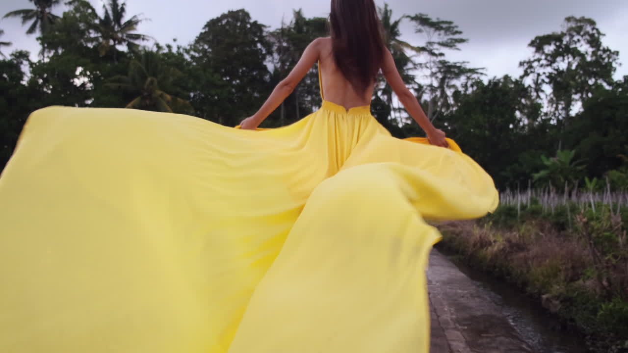 женщина в желтом платье идет по рисовому полю.