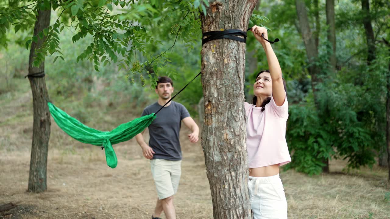 una pareja montando una hamaca en el bosque.