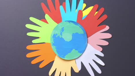 close-up van handen samen met een globe gemaakt van kleurrijk papier op een grijze achtergrond met kopieerruimte