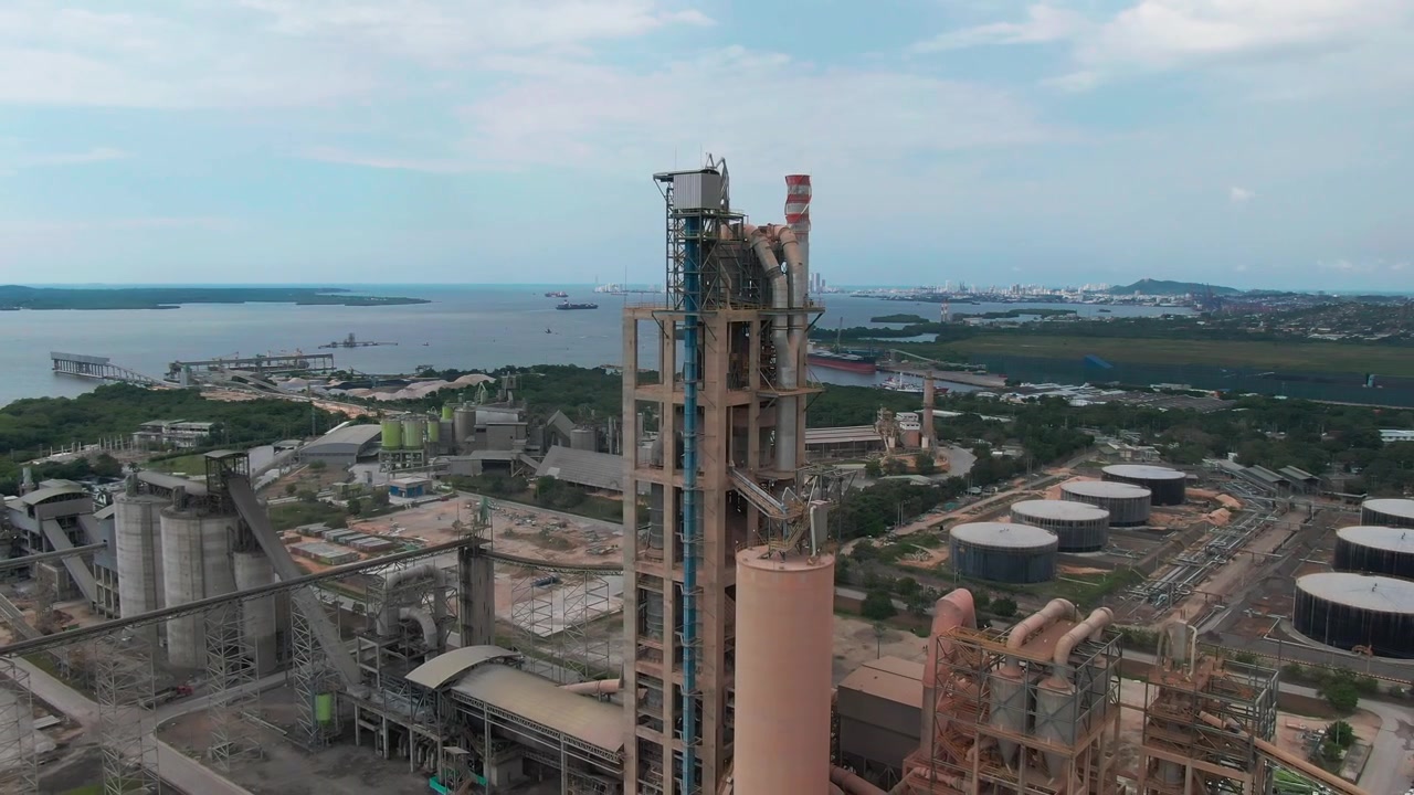 Droneoptagelser af et stort industrielt cementanlæg med siloer og skorstene, beliggende ved kysten nær Cartagena, Colombia.
