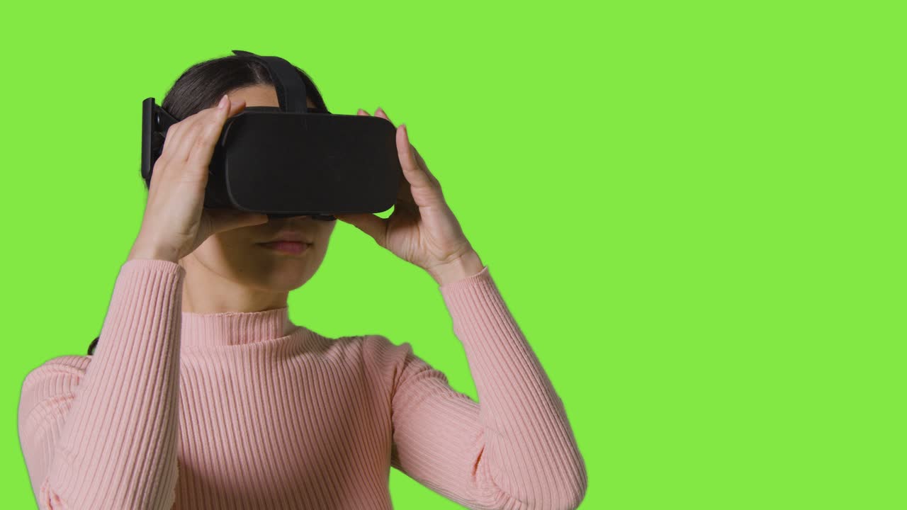 mujer poniendo auriculares de realidad virtual y mirando a su alrededor contra el fondo del estudio de pantalla verde