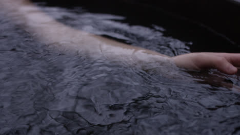 Female-hand-moves-through-water-in-outdoor-hot-tub