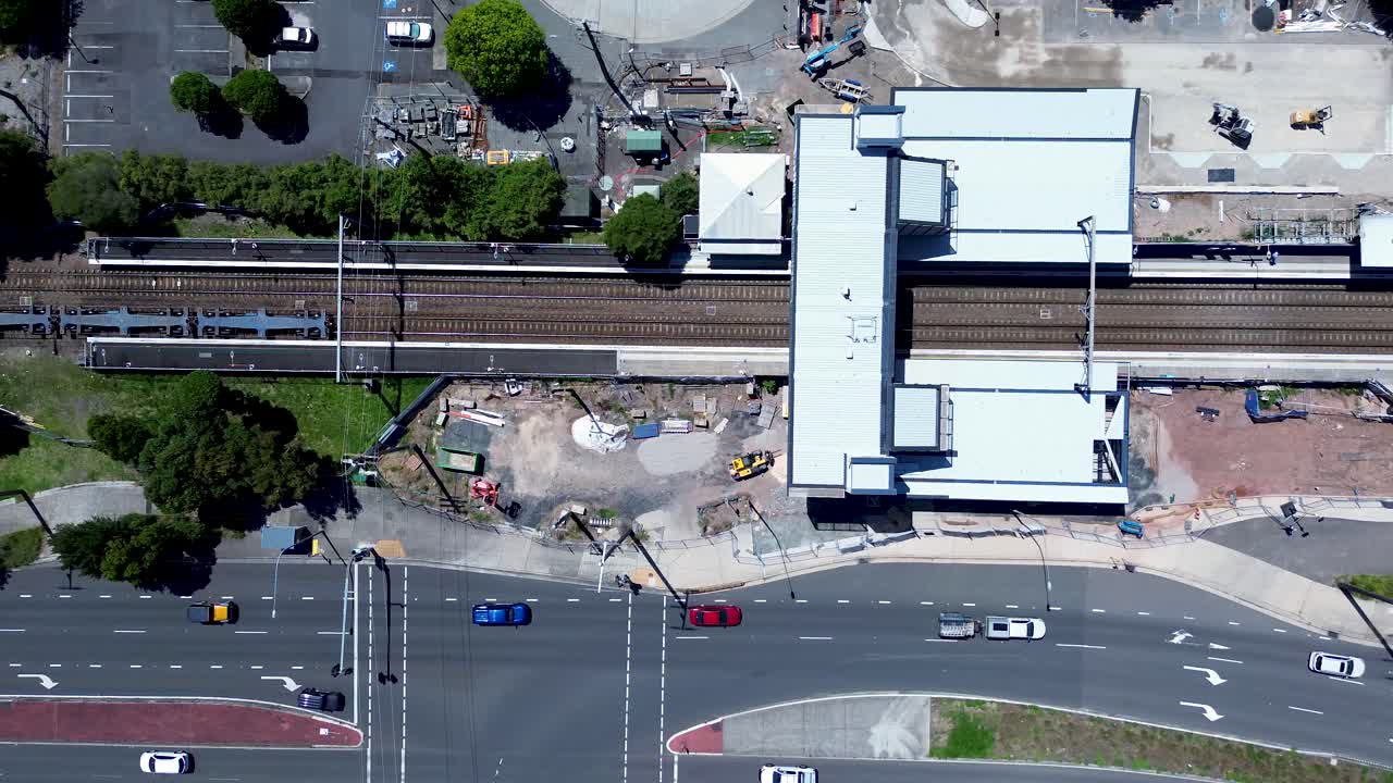 Drone aerial landscape of coal train carriage on railway tracks passing through Tuggerah station platform with traffic intersection car vehicles Central Coast tourism transport travel