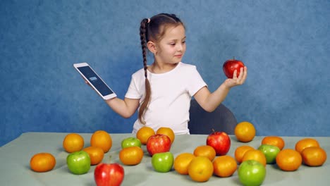 choosing between apple and tablet. cheerful smiling girl sitting at table with fruits and tablet