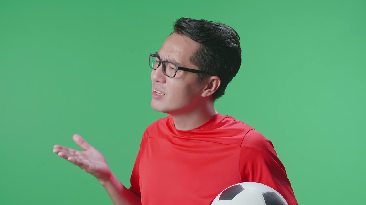 초록색 스크린 배경에서 축구를 응원하는 동안 패자를 조롱하는 공을 가진 아시아 남자의 가까운 측면 시각