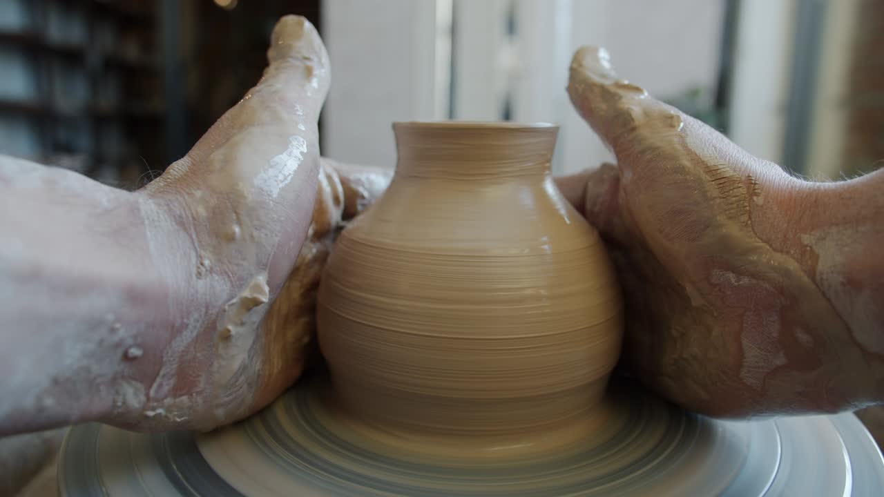 Cinemagraph loop of ceramic pot rotating on potter's wheel in dirty hands of craftsman