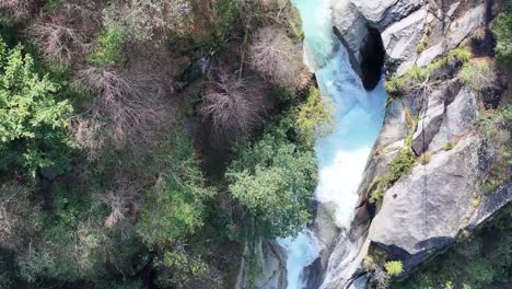 Una-Vibrante-Cascada-De-Color-Turquesa-Que-Atraviesa-Un-Terreno-Rocoso-Rodeado-De-Exuberante-Vegetación,-Vista-Aérea