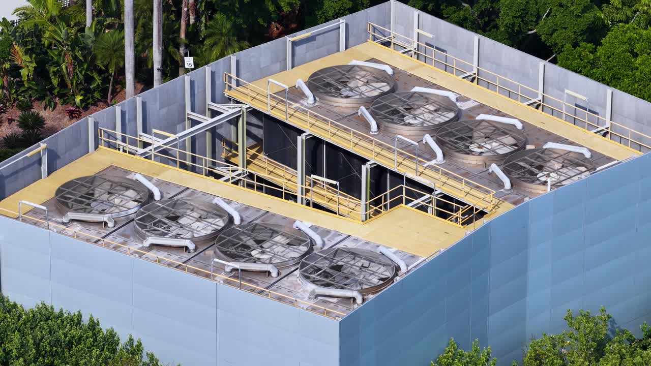 Aerial footage of a cooling tower with rotating fans, surrounded by greenery. Bright daylight enhances the industrial setting