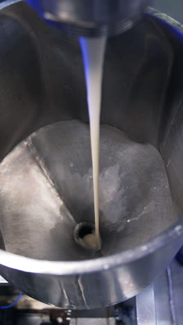 condensed milk streaming from a tube into a metal container. close up. food factory automated line. view from above. vertical video
