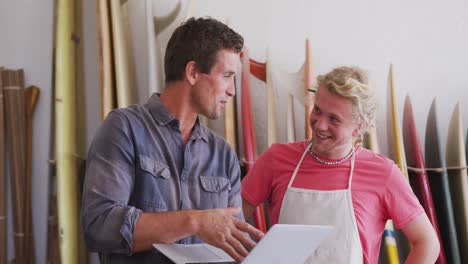 two caucasian male surfboard makers working on projects using a laptop computer