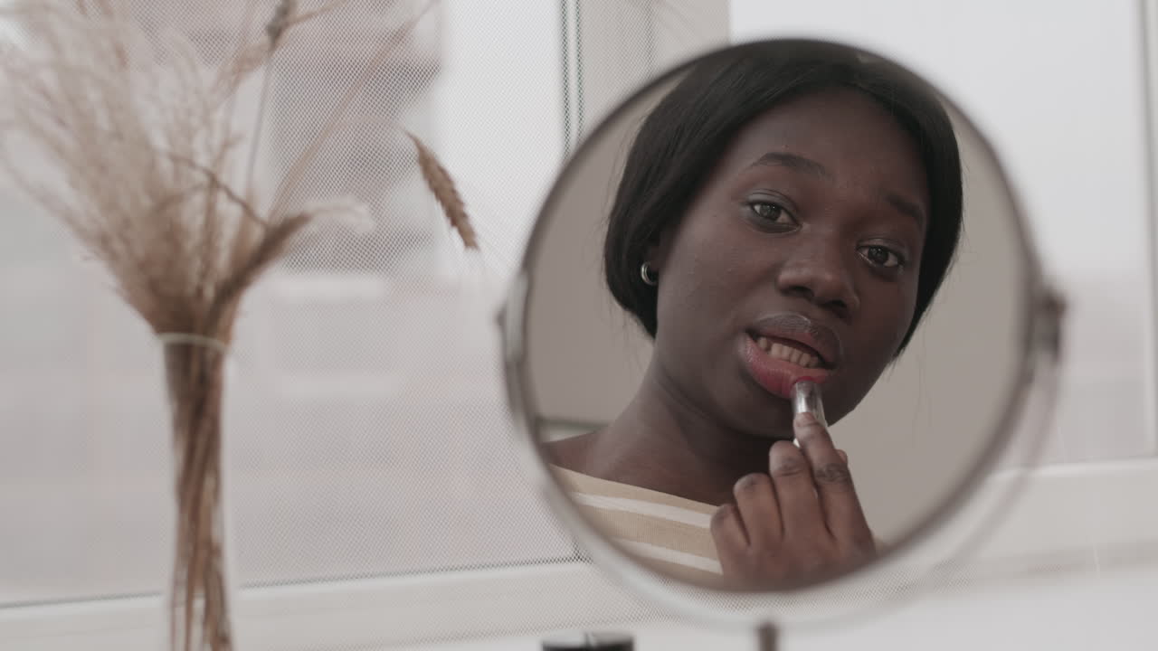 Reflection of Young African Woman Applying Lipstick