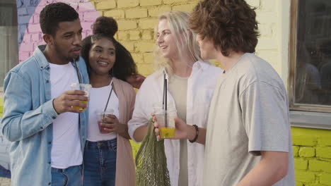 group of  young friends taking selfies together and having fun outdoors, while holding their fresh drinks in plastic cups