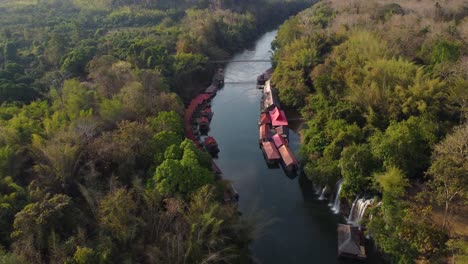 Un-Dron-Giratorio-De-Un-Río-En-Tailandia-En-Medio-De-La-Jungla,-Con-Cascadas-Y-Un-Pueblo-Flotante-Al-Lado-Del-Río