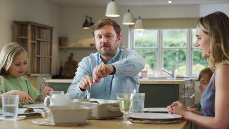 father serving food as family sit around table at home enjoy meal together