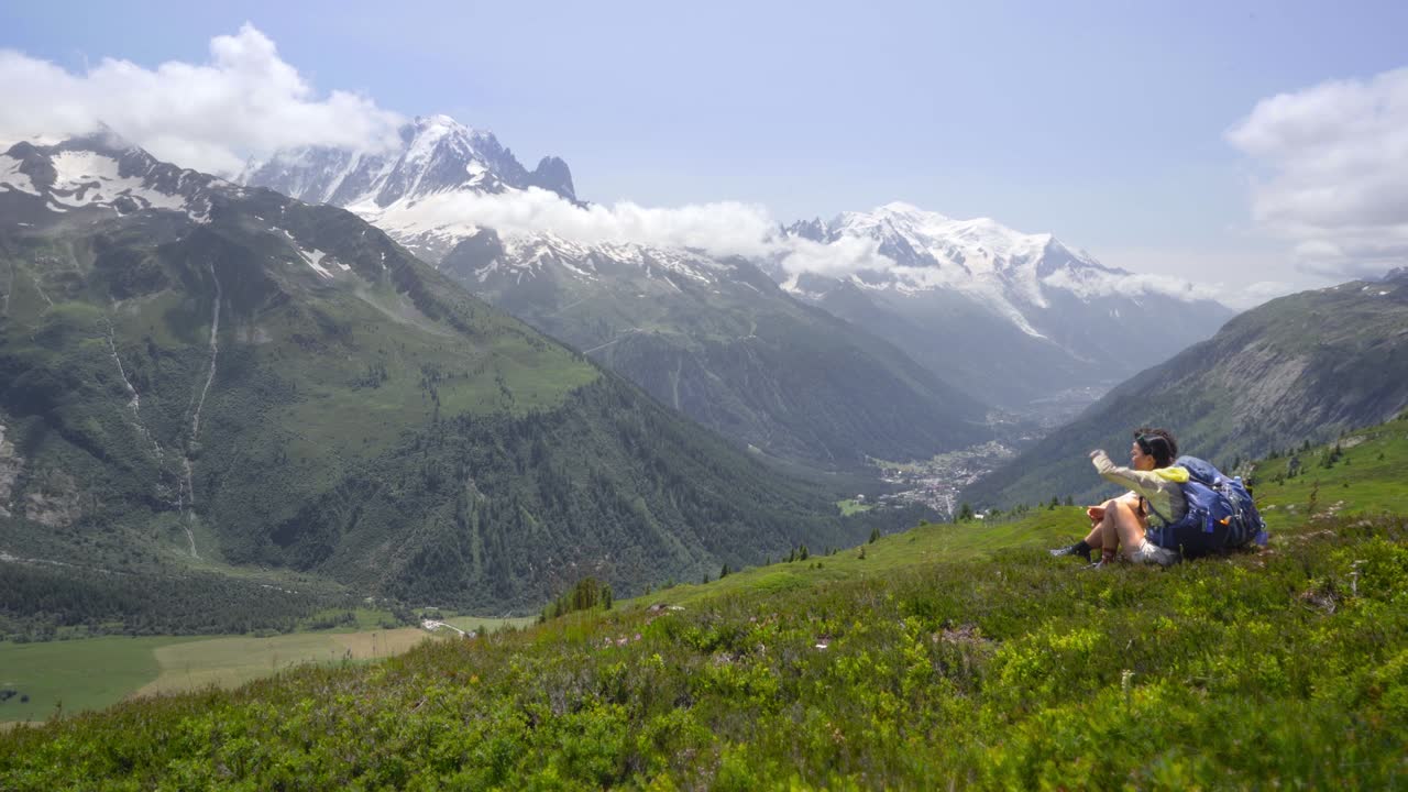 vista panorámica de una pareja de excursionistas en la pista de senderismo de mont blanc, rodeada por los altos picos de los alpes en medio de un campo de hierba