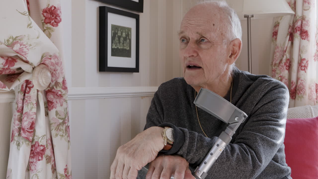 Elderly man sitting indoors with a crutch