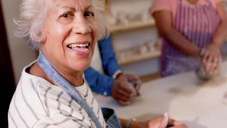 Happy-biracial-female-potter-with-gray-hair-shaping-clay-with-hands-in-pottery-studio,-slow-motion