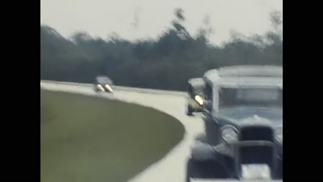 group of classic cars driving down a historic road in a 1970s american old car show. circa usa - 1970s: a nostalgic scene of a group of vintage cars from the 1970s, driving in unison down a historic road at an old car show in the usa.