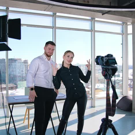 young bloggers recording video about their business. creative young couple shooting video in front of professional camera in office with panoramic windows