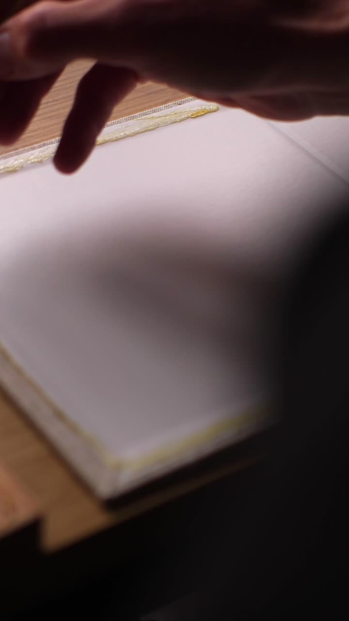 Craftsman applies glue to handmade wooden box, shot over shoulder in dark room, vertical slow motion