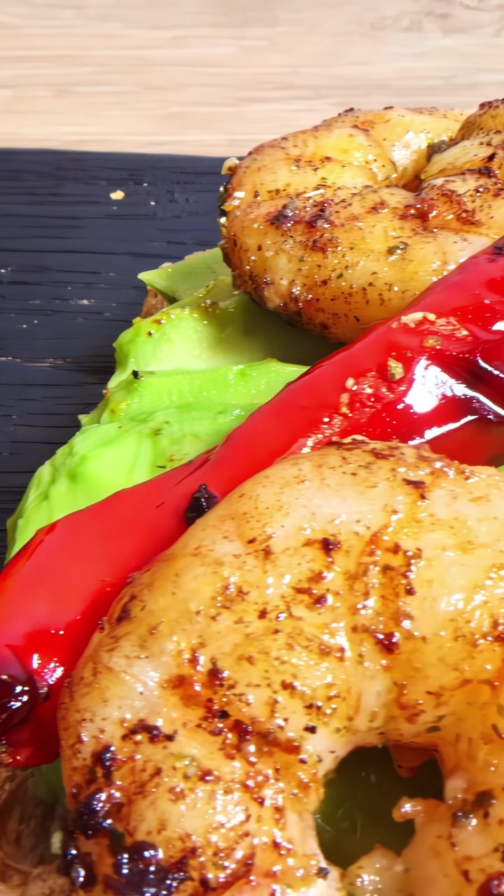Toast salutari con avocado, gamberi grigliati e peperoni arrostiti che scivolano su un tagliere di legno scuro.