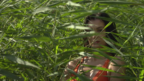 pretty young woman hiding outdoor behind green nature plants on sunny day,slow motion