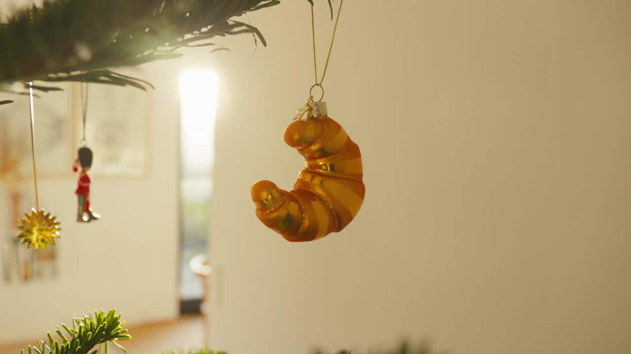 un ornamento de croissant dorado colgando de un frondoso árbol de navidad