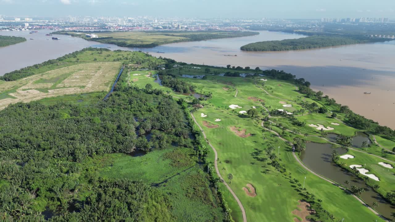 Breathtaking aerial footage of a vibrant golf course by the Saigon River, Bình Dương. Balanced composition captures lush greens against urban skyline under clear skies, ideal for serene views