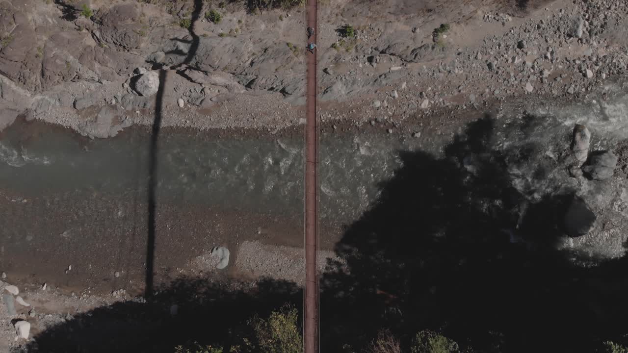 dos personas caminando sobre un puente colgante de alambre de metal que se extiende sobre un río rocoso en una región remota de filipinas