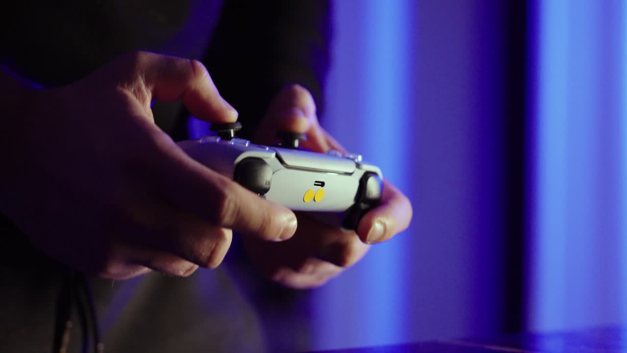 Close-up of hands using a game controller under blue ambient lighting at night. Concept for gaming lifestyle, streaming, esports, and home entertainment