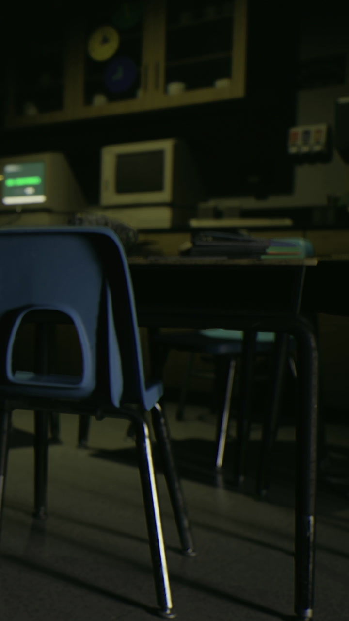 Chair by a table in a classroom with old computers and dark lighting