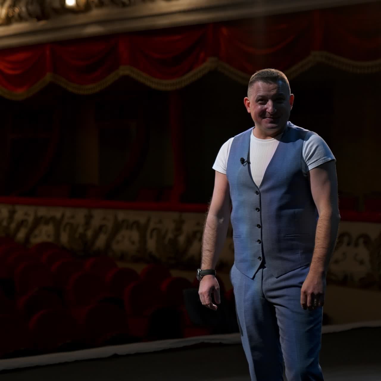 Performer points on a watch from stage and announces performances in theater. Beginning of theater season after covid-19