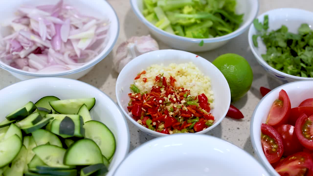 A hand selects fresh lime among colorful salad ingredients on a kitchen countertop under bright lighting