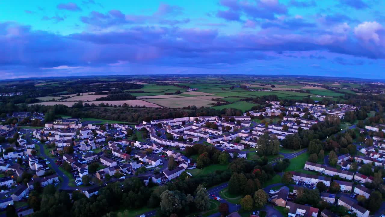 Aerial view of a peaceful residential town at sunset, surrounded by fields and farmland. Blue hour tones blanket the sky and landscape in this scenic rural community