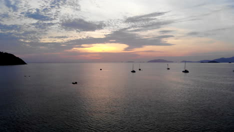 Aerial-view-of-boats-anchored-on-a-peacefull-ocean-with-a-colorfull-sunset