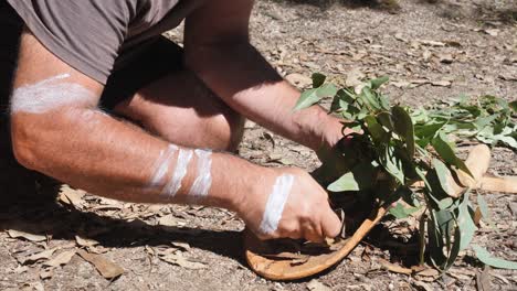 Australian-Aboriginal-Smoking-Ceremony,-man-creates-smoke-from-burning-leaves-on-a-traditional-wooden-bowl-as-part-of-an-ancient-indigenous-custom